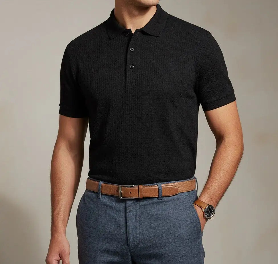 Man wearing a black BCI Cotton polo shirt and blue pants with a brown belt against a neutral background