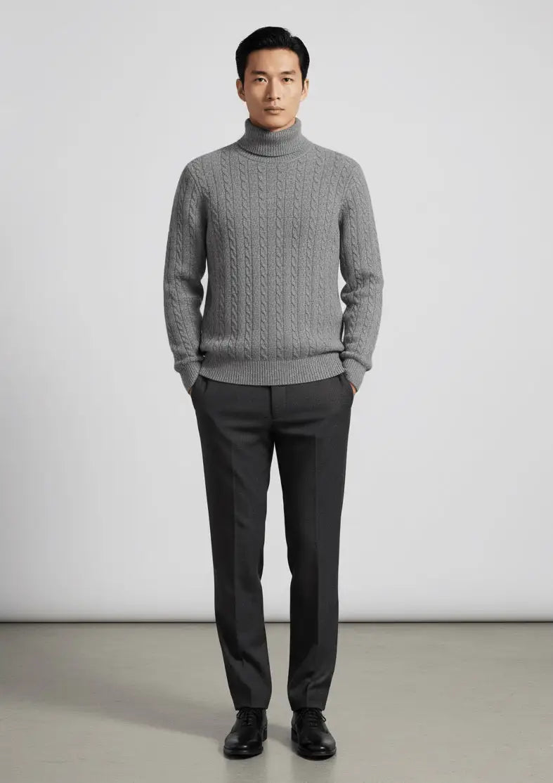 Man wearing a gray cable knit sweater and dark pants against a plain background