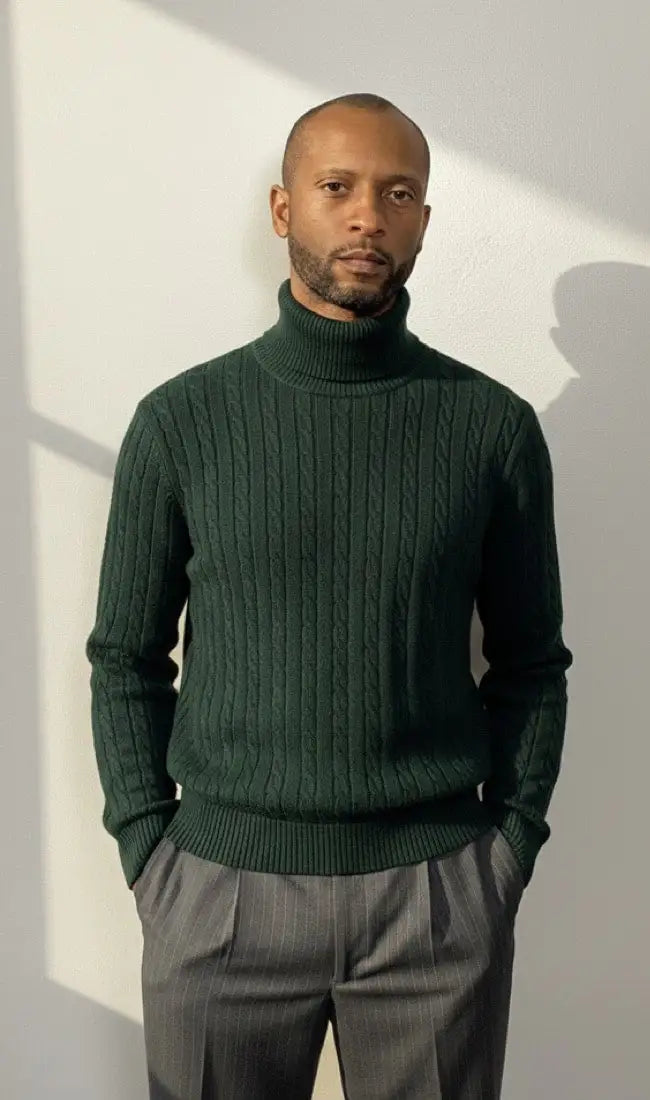 Handsome man wearing a green turtleneck sweater and gray pants against a white wall