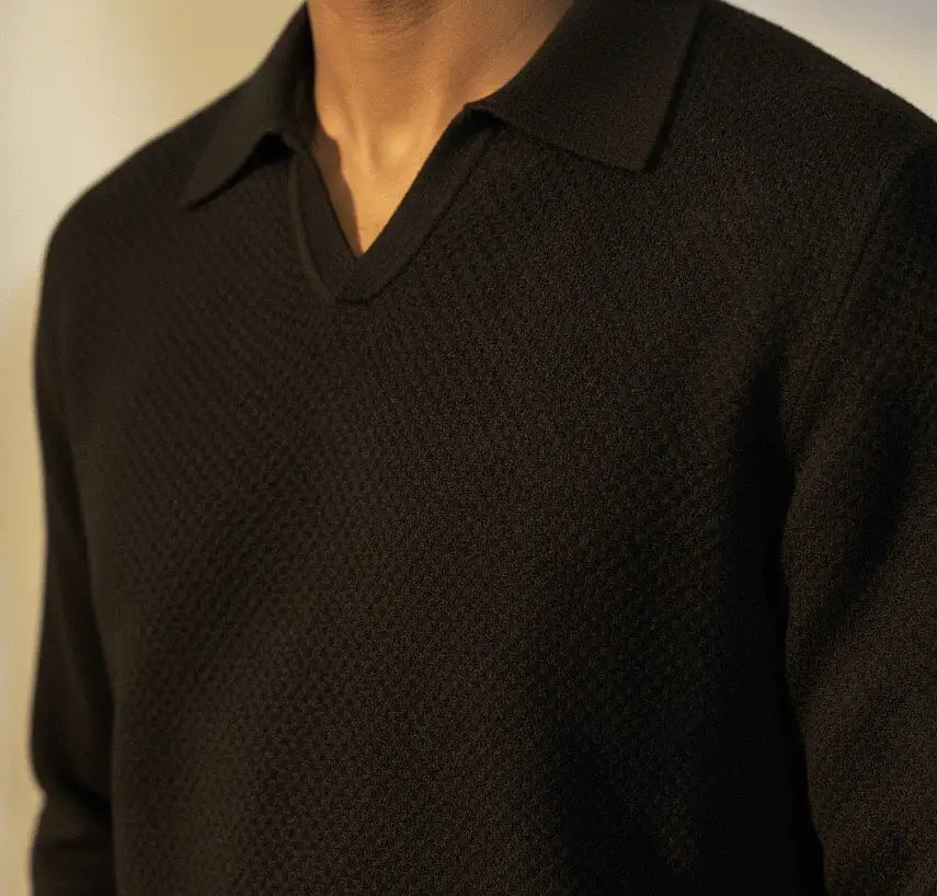 Close-up of a person wearing a black textured long sleeve v-neck Jacquard knit polo against a neutral background