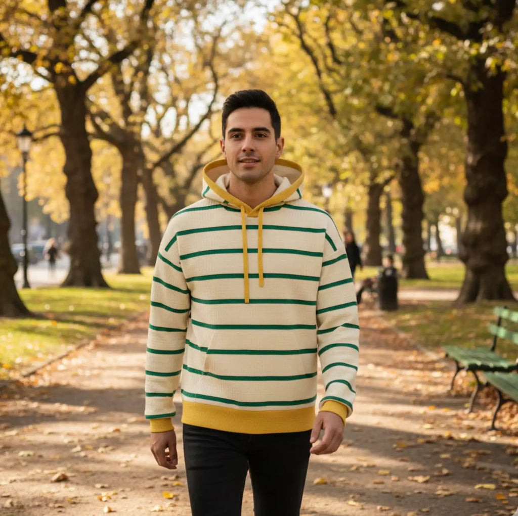 Man wearing a Beige, yellow and green striped hoodie in a park with trees and benches in the background