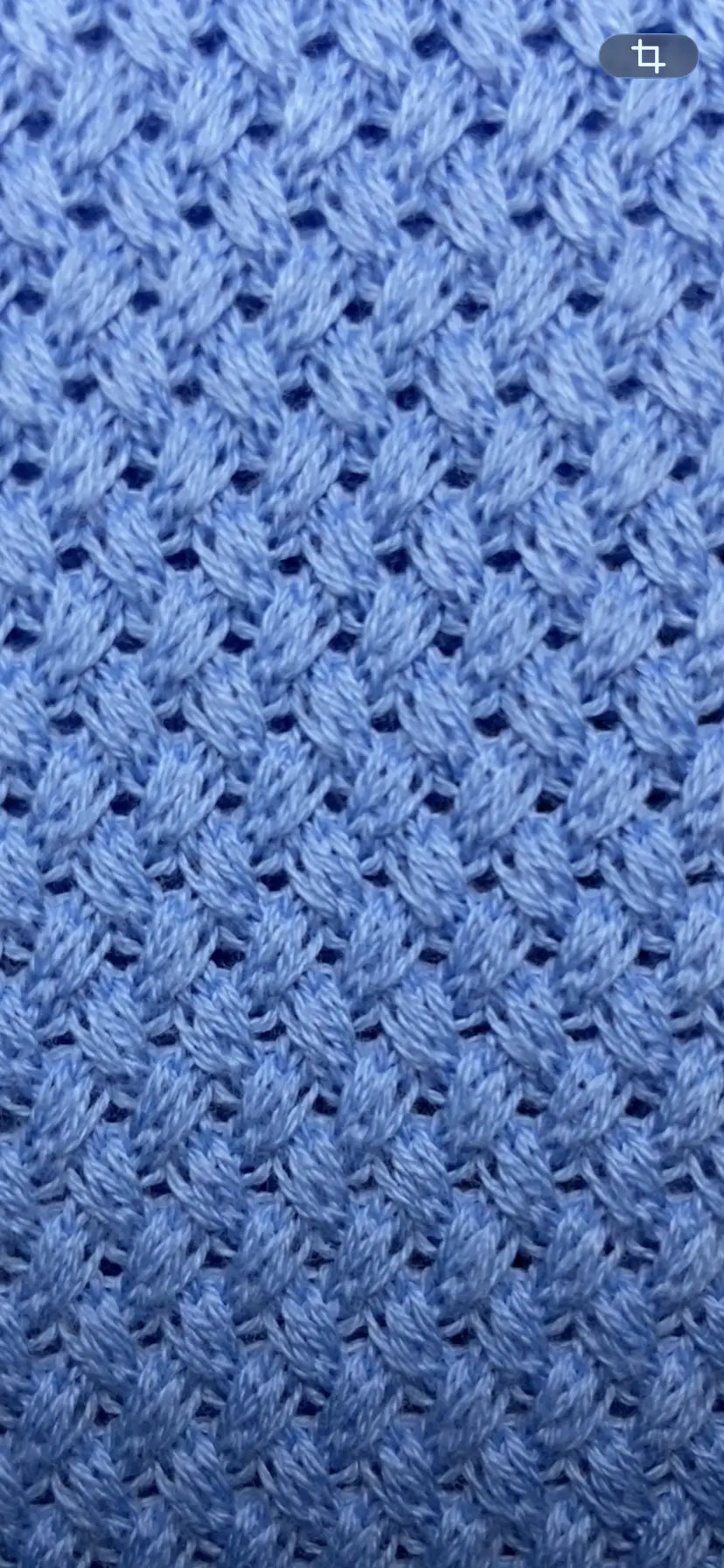 A close-up of a blue textured knit fabric with a repeating diamond pattern.