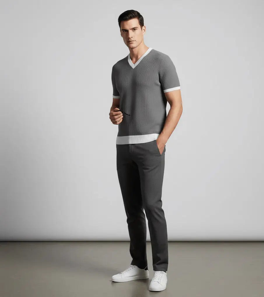 Man wearing a gray V-neck shirt and dark pants against a plain background
