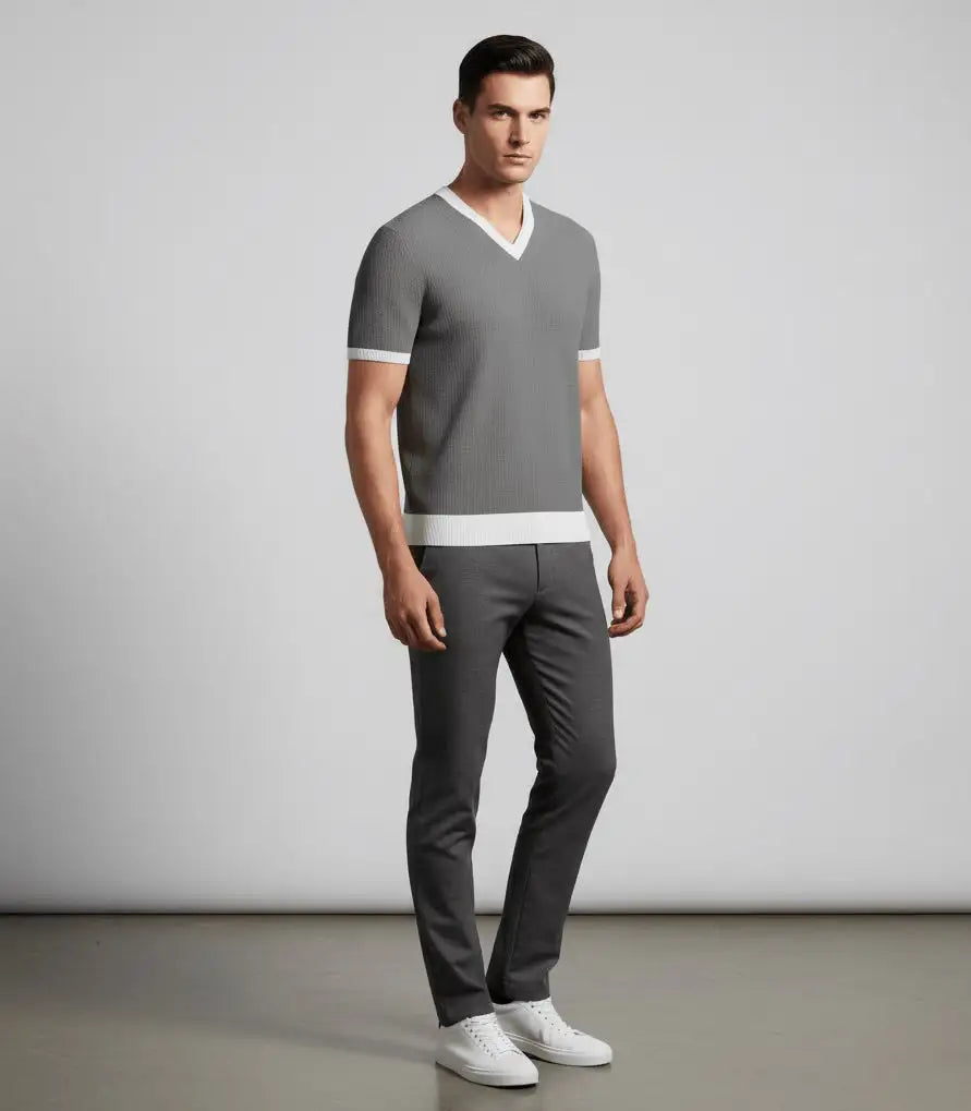 Man wearing a gray V-neck sweater and pants with white shoes on a plain background